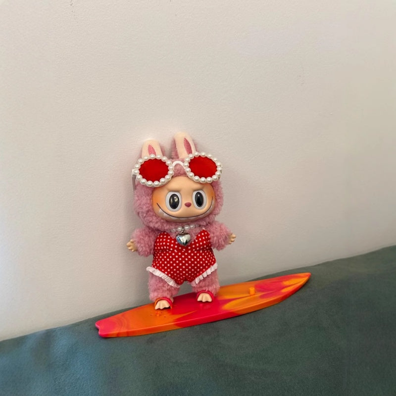 Labubu doll dressed in red surfing outfit standing on orange-red surfboard. Outfit fits all Labubu dolls, doll not included.